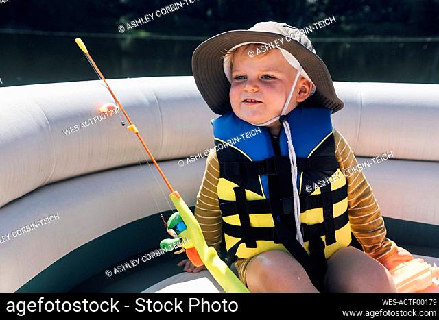 Cute little baby boy wearing hat sitting on boat with fishing rod