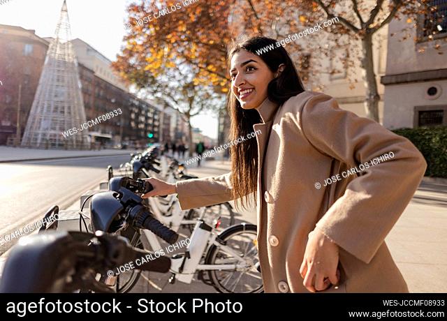 Happy young woman renting bicycle on sunny day