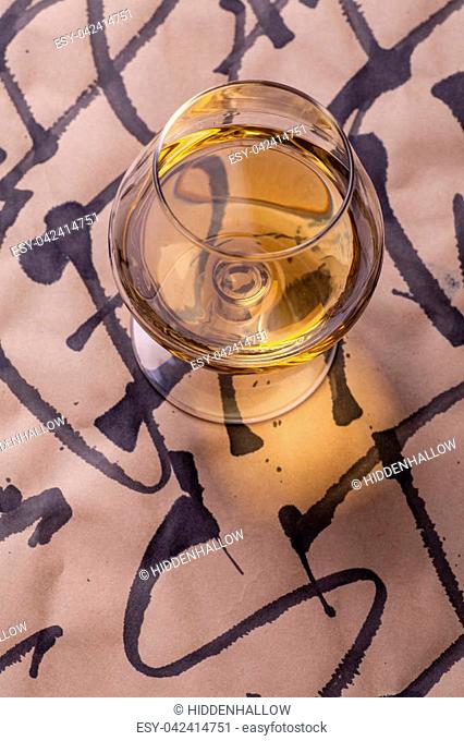 Snifter glass with brandy standing on a sheet of paper with calligraphy signs written all over it