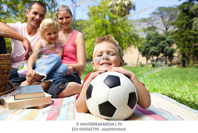 Smiling boy holding a soccer ball with his family in the background