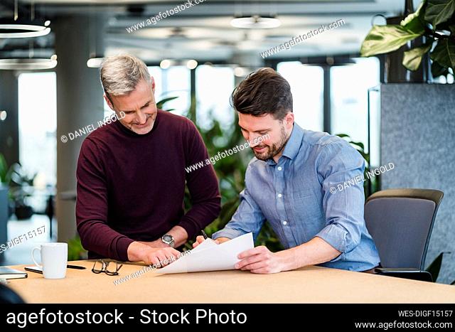 Businessman and male colleague discussing over documents at table in office