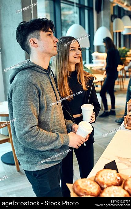 Friends doing shopping in a coffee shop. Young man and woman having chat while picking out the pastry, bakery's goods and hot drinks standing at counter in a...