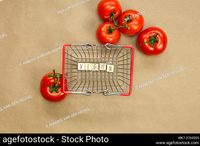 Vegan written on wooden cubes surrounded with vegetables in shoppin basket top view with craft paper background, Vegan, Healthy food, Vegetarian concept
