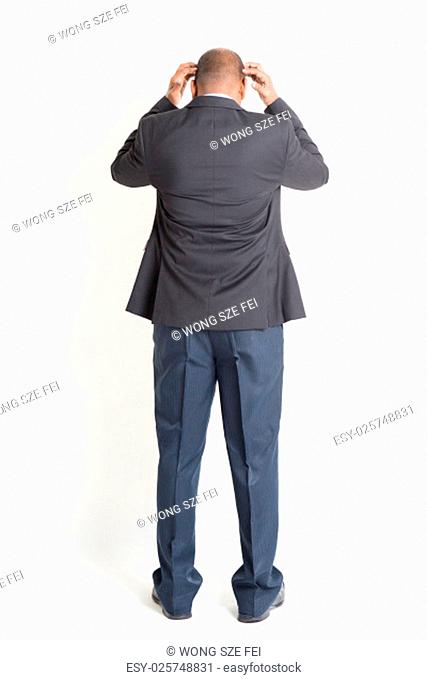 Rear view full body mature Indian business man hands scratching head and running out of idea , standing on plain background