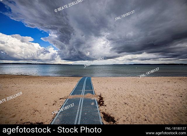 Dramatic storm clouds over the deserted beach of Holnis/Glücksburg. A plastic runway for wheelchair users leads to the tide line