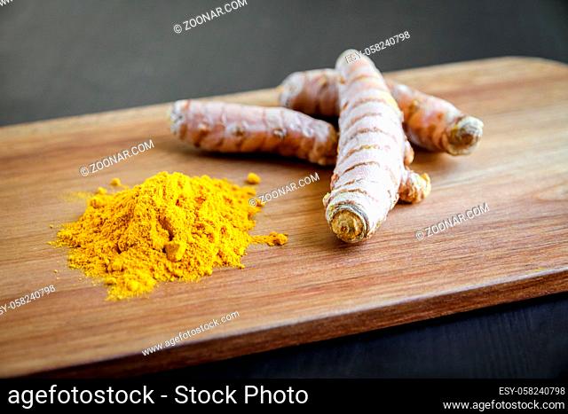 Turmeric root and spice powder on a wooden cutting board