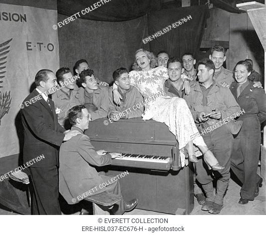 Actress Marlene Dietrich singing for a group of GI's in France. Joey Faye (left), and Jerry Cummings, pianist, accompanied Miss Dietrich, Oct