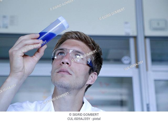 Male scientist looking up at sample in plastic bottle in lab
