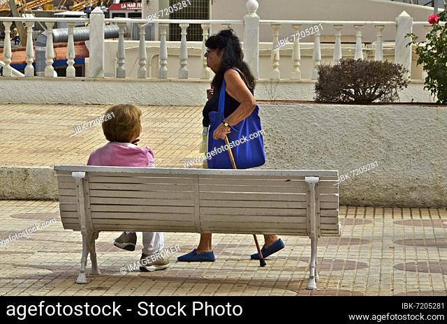 Woman on bench watching passing woman with walking stick, Villaricos, Andalucia, Spain, Europe