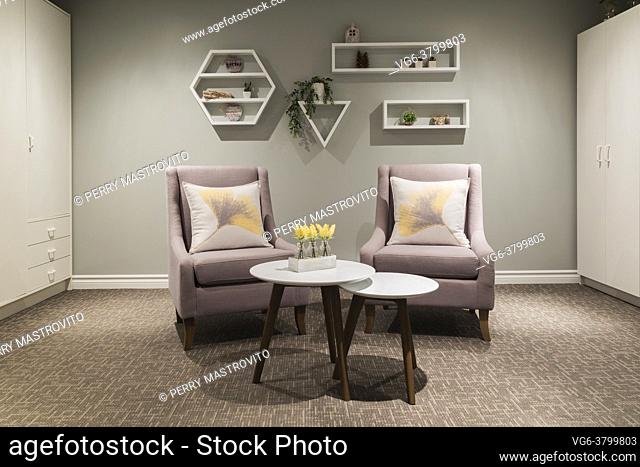 Grey cloth upholstered armchairs and white round tables and storage cabinets in den in basement of contemporary home, Quebec, Canada