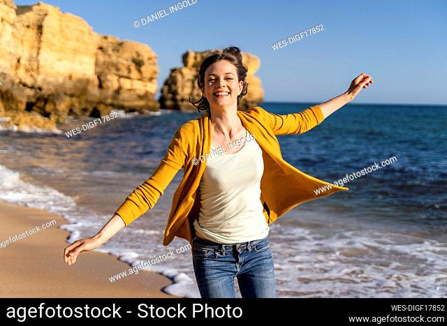 Happy woman with arms outstretched enjoying in front of sea at beach