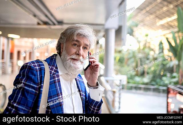 Mature man with white beard looking away while talking on smart phone at station