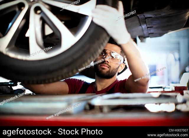Male mechanic working under car, examining tire in auto repair shop