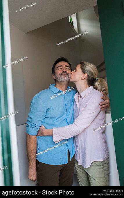 Mature woman kissing husband standing at home