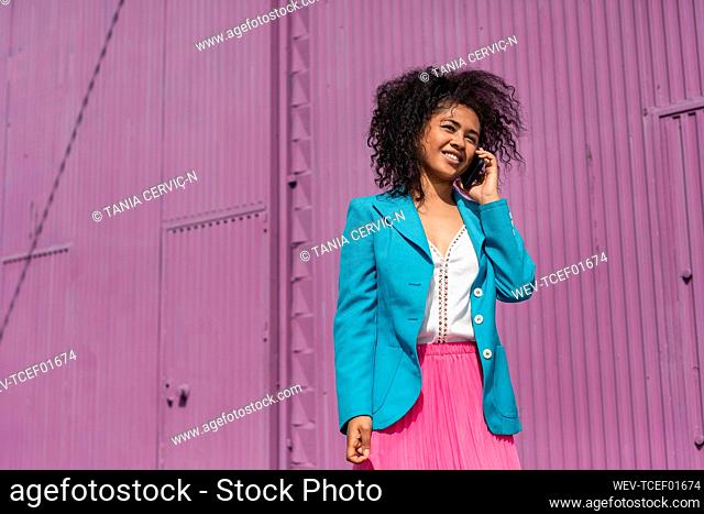 Smiling woman with Afro hairstyle talking on phone during sunny day