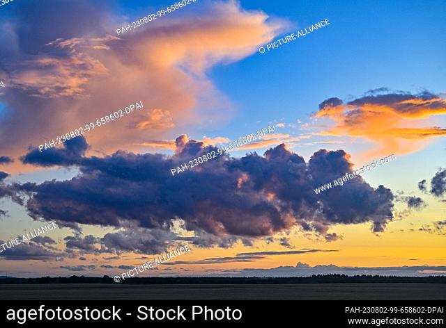 01 August 2023, Brandenburg, Jacobsdorf: Clouds over the landscape are bathed in a warm light from the sunset. Photo: Patrick Pleul/dpa