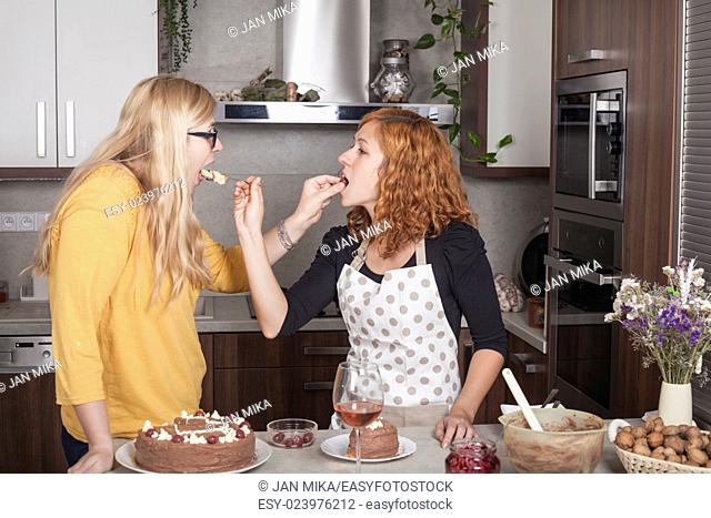 Girlfriends feeding each other with a cake and cooking together in the kitchen at home