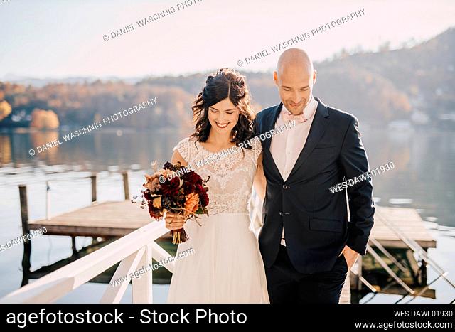 Bride and groom walking on jetty over lake
