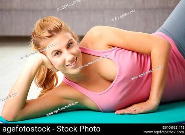 Young woman doing exercises lying on fitness mat in living room, smiling