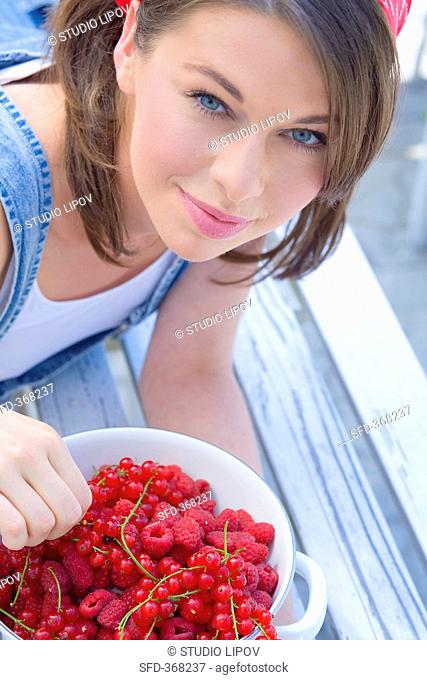 Young woman holding bowl of redcurrants and raspberries
