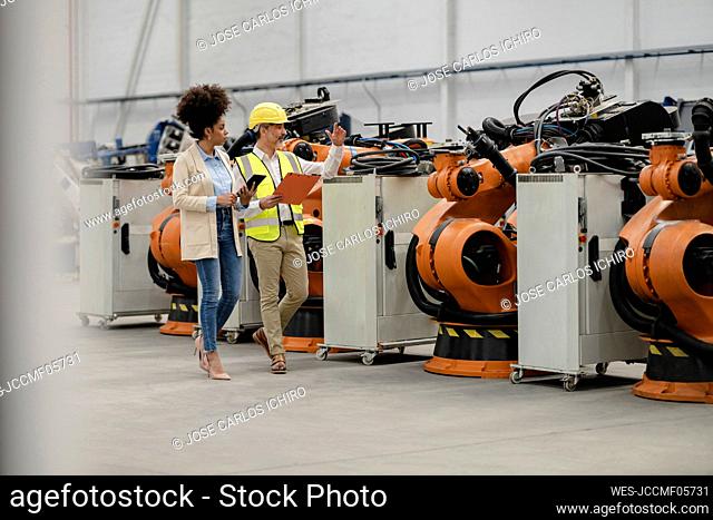 Businesswoman holding tablet PC discussing with engineer walking in factory