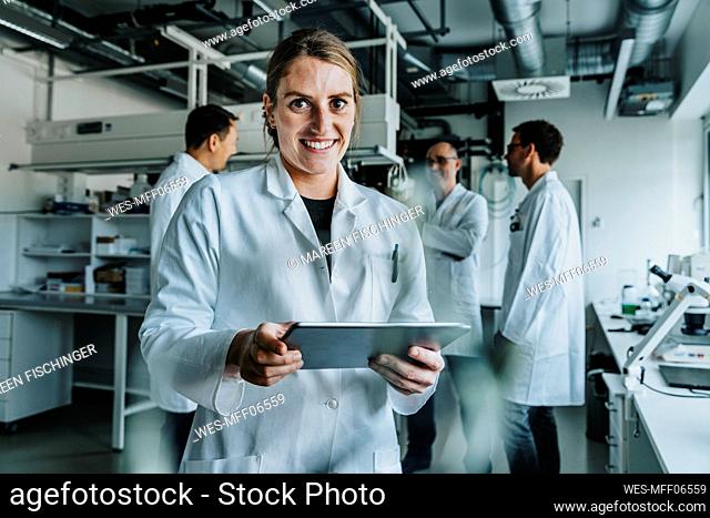 Smiling woman using digital tablet while standing with coworker in background at laboratory