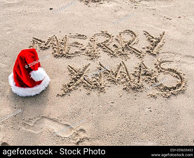 Merry Xmas greetings hand-written on the beach sand with red santa Claus hat