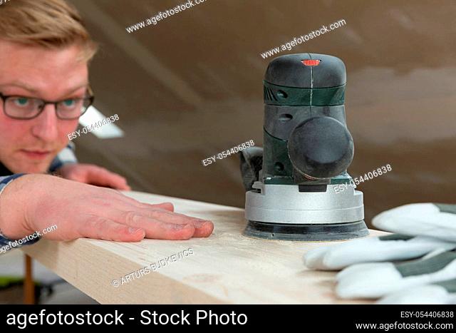 Worker grinds the wood with orbital sander machine in a natural light