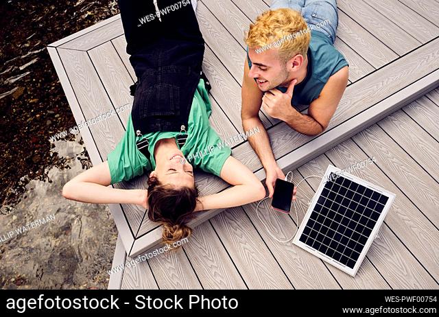 Smiling couple relaxing on patio with smart phone getting charged by solar panel