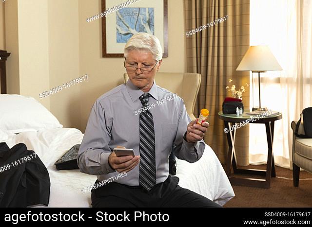 Mature Caucasian man sitting on edge of bed in a hotel room, using cell phone to check prescription medication