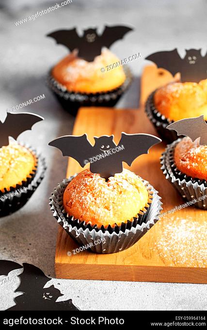 Halloween pumpkin muffins in black capsules decorated with cardboard bats. Festive Halloween cupcakes. Close-up view of delicious spooky halloween muffins on...