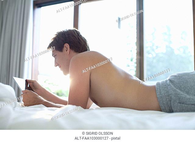 Man lying in bed using digital tablet