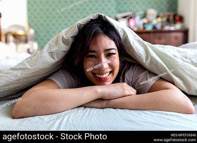 Happy woman relaxing on bed with blanket at home