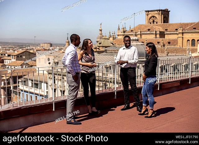 Smiling male and female entrepreneurs discussing on rooftop of office building during break