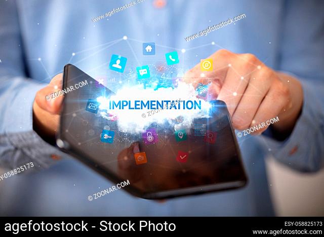 Businessman holding a foldable smartphone with IMPLEMENTATION inscription, technology concept