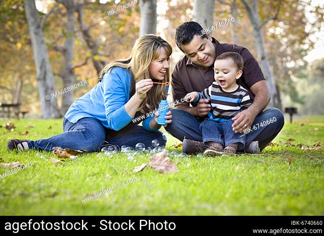 Happy young mixed-race ethnic family playing with bubbles in the park