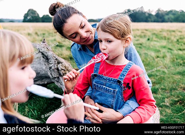 Woman looking at girl eating lollipop in park