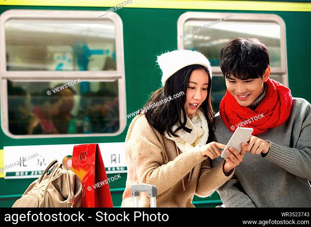 Young lovers see mobile phone in the railway station