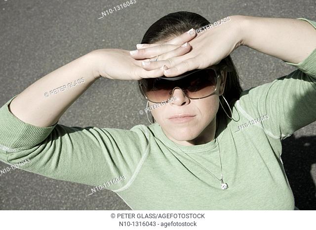 Young woman, wearing sunglasses, blocking the sun with her hands