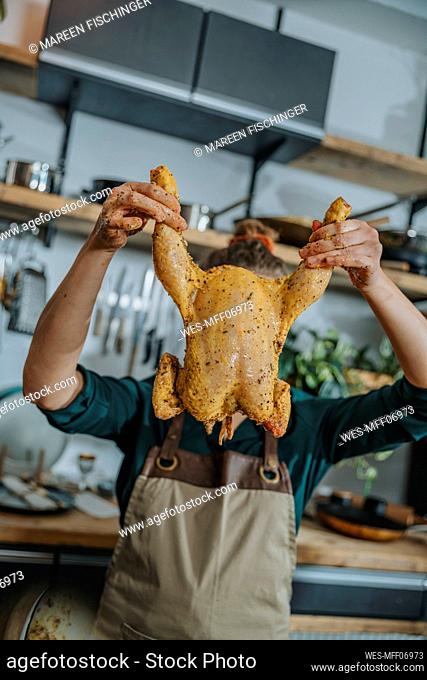 Young female chef holding marinated chicken meat while standing in kitchen