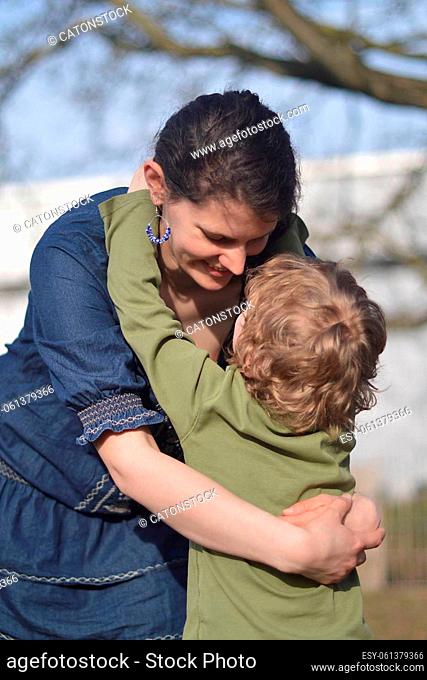 Happy mother holding little child in her arms with love in a garden outdoors in summertime