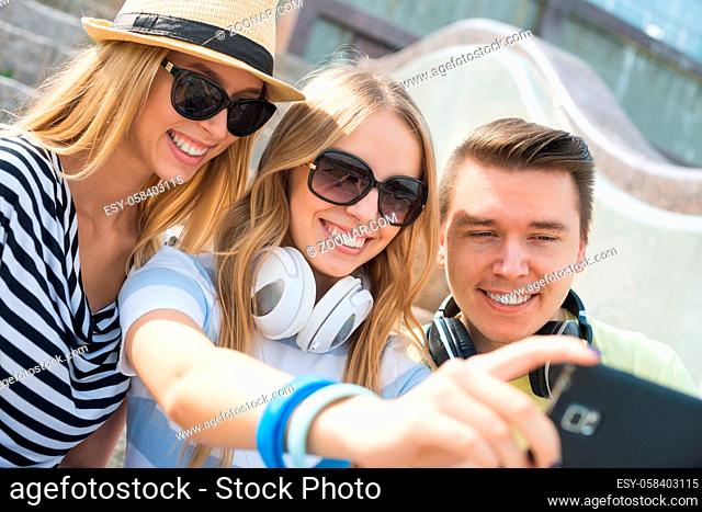 Three young happy people sitting outdoors and making selfie