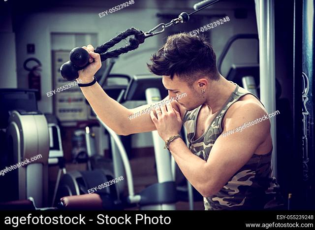 Young man training on gym equipment, pulling handle on cables