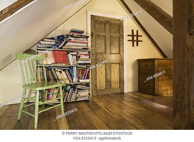 Attic room with green wooden sitting chair next to antique bookcase and stressed finish closet door inside an old 1835 fieldstone house