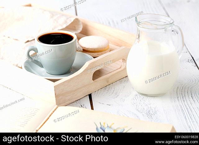 Cup of coffee and macaron cakes on tray on white wooden table
