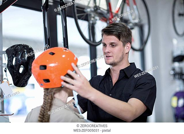 Young salesman putting bicycle helmet on woman's head