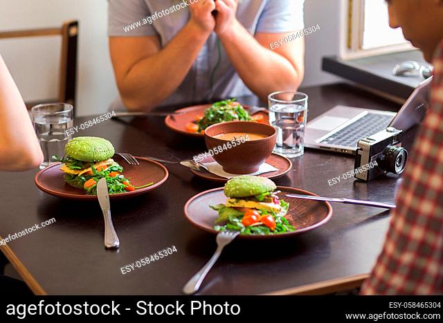 Closeup image of people sitting in vegan cafe or restaurant and eating tasty vegetarian sandwich with tofu, tomatoes, salad and cucumber on plate represented on...