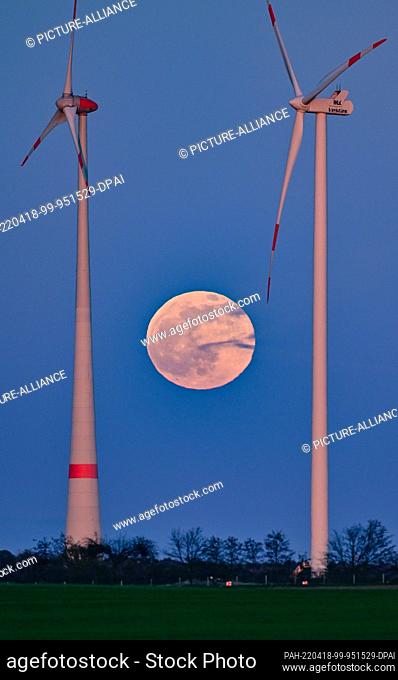 16 April 2022, Brandenburg, Petersdorf: The full moon shines at dusk between the masts of wind turbines in East Brandenburg. Photo: Patrick Pleul/dpa