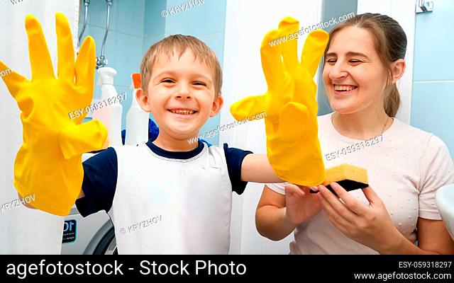 SMiling toddler boy wearing yellow rubber gloves laughing while doing housework and home cleanup