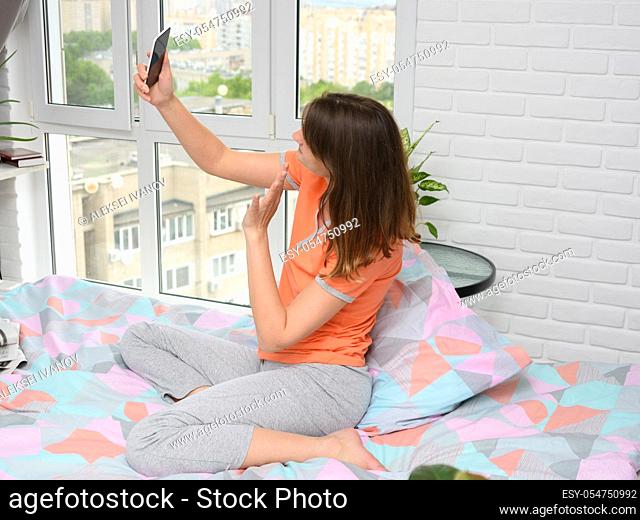 Girl sitting on bed at home happily communicates with her friend via video calling